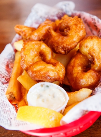 A basket of breaded and fried shrimp with tartar sauce and lemon wedgeの写真素材
