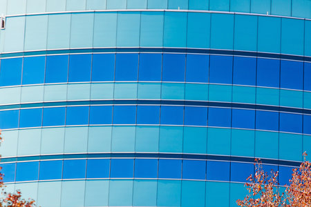A curved, green and blue office building in autumn