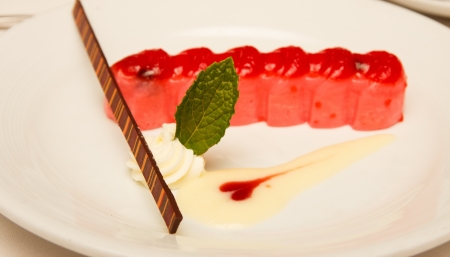 A dessert of strawberry mousse with chocolate straw, whipped cream and a mint leaf garnishの写真素材