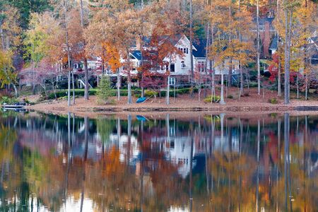 A nice lakeside home with calm water reflecting autumn treesの写真素材