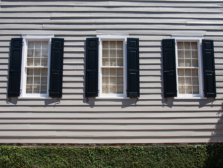 Three windows in wood siding home with black shuttersの写真素材