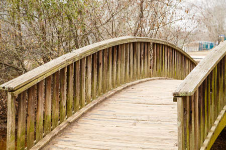 Odl wooden bridge curving over a small stream in a parkの写真素材