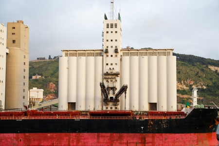Old red and black freighter docked at an industrial port ready to loadの写真素材