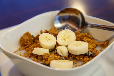 A bowl of raisin bran with spoon and bananas