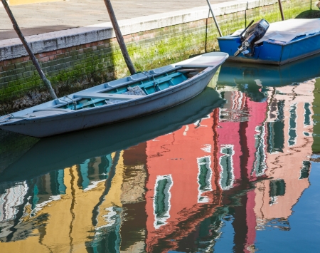 Reflection of colorful homes in a canal with blue boats in Burano, near Venice, Italyの写真素材