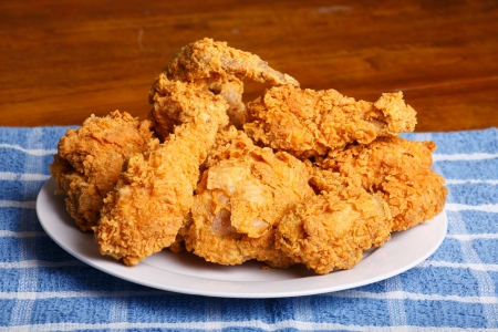 A plate of fresh, hot, crispy fried chicken on a blue plaid towel on a wood tableの写真素材