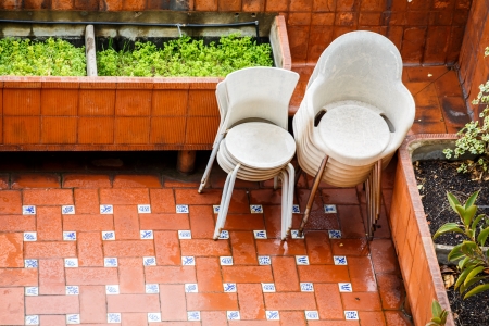 Stacks of platic chairs on a wet tile patio in the rainの写真素材