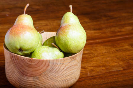 Green pears in a wood bowl in window light on wood tableの写真素材