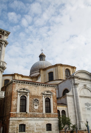 Old burial house by church on canal in Venice under nice skiesの写真素材