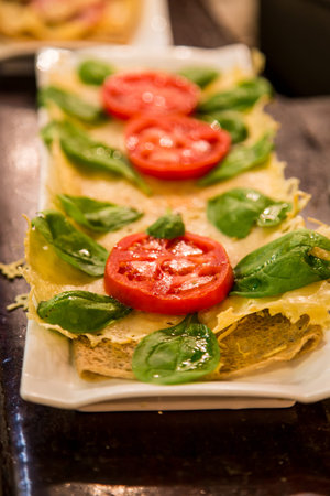 Tapas appetizer of fresh, red, ripe, sliced tomatoes, basil, and oil on cheese and breadの写真素材