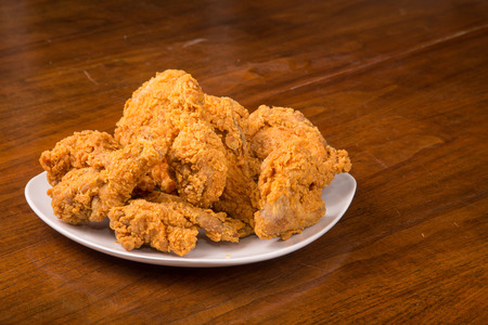 A white plate of fresh, hot, crispy, fried chicken on a wood tableの写真素材