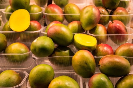 Whole and Cut Mangoes in plastic bins in a fruit marketの写真素材