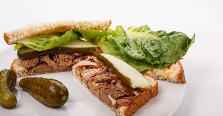 A chopped pork sandwich with lettuce and pickles on a white plateの写真素材