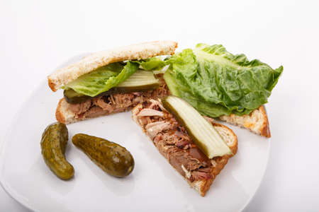 A chopped pork sandwich with lettuce and pickles on a white plateの写真素材