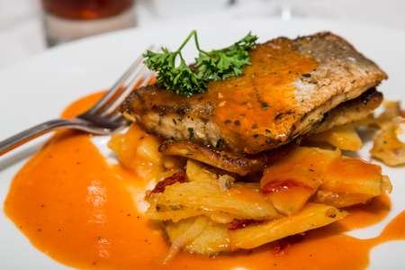 A meal of broiled fish on baked potatoes in a sauce garnished with parsleyの写真素材