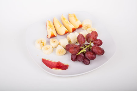 A fruit plate with sliced apples, sliced bananas and a bunch of red grapesの写真素材
