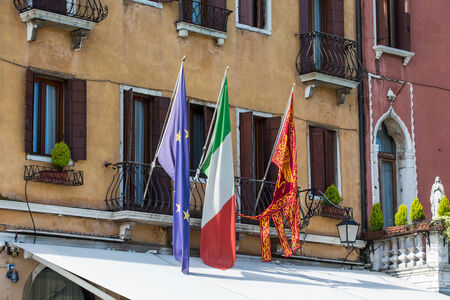 Old Venice hotel with colorful flags over canopyの写真素材