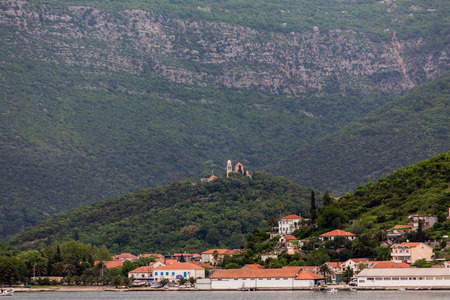 Old buildings with red tiled roofs in Kotor with Church on Green Hilltopの写真素材
