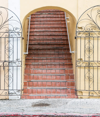 An old yellow plaster building with worn, red tile steps trhough an archway