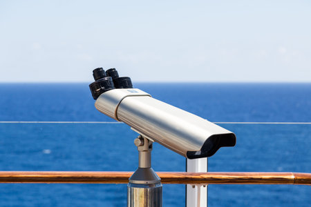 A silver spotting scope on the deck of a ship overlookng blue seas