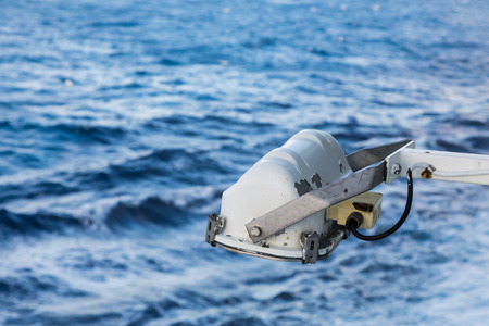 An old white spotlight on a ship overlooking deep blue waves in oceanの写真素材