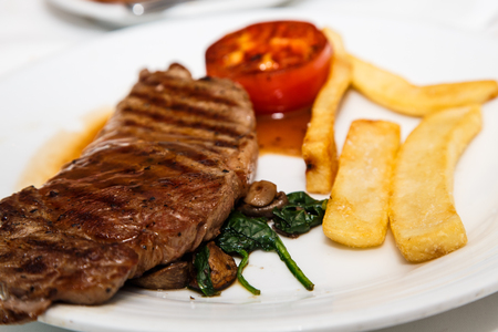A grilled new york strip steak with french fried potatoes and a grilled tomato halfの写真素材