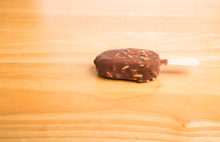 A cold, tasty, ice cream bar covered in chocolate and almonds on a wood tableの写真素材