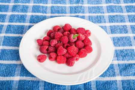 White plate of luscious, red, ripe raspberries