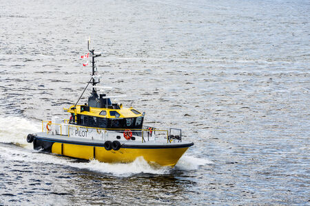 A bright yellow pilot boat speeding across a calm blue harborの写真素材