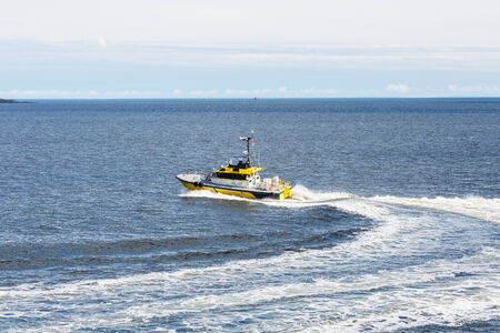 A bright yellow pilot boat speeding across a calm blue harborの写真素材