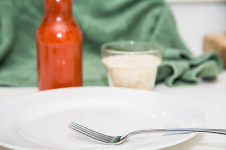 An empty plate on a counter with fork with hot sauce and cheese in backgroundの写真素材