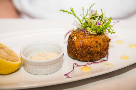 Fresh crab cake with sauce and half lemon garnished with greens