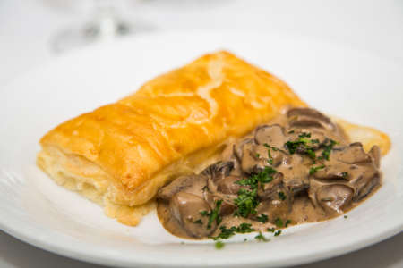 A gourmet appetizer of mushrooms and puff pastry on a white plateの写真素材