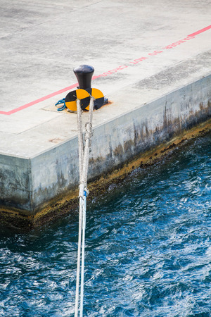 White Ship's rope tied to black and yellow bollard on a concrete pierの写真素材