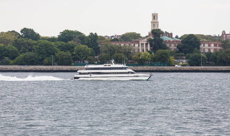 A large white ferry cruising past the old Fort Hamilton high school on the Hudson River between New York and New Jerseyの写真素材