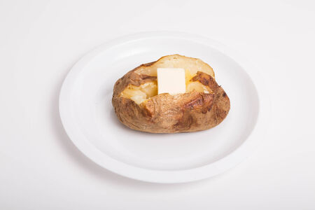 A hot baked potato, cut open and buttered on a white plate and backgroundの写真素材