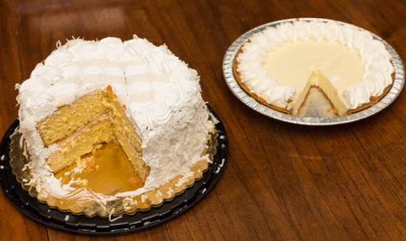 A fresh baked coconut cake in a plate on a wood table alongside a lemon meringue pie