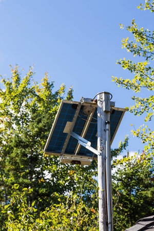 A small solar panel on a wood pole with green trees and blue sky in background