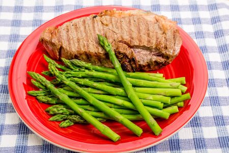 Grilled strip steak on a red plate with asparagusの写真素材