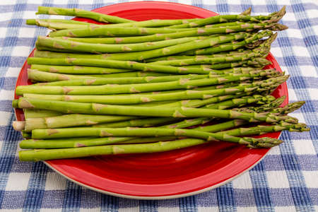 A fresh bunch of raw asparagus on a red plate and blue plaid tableclothの写真素材