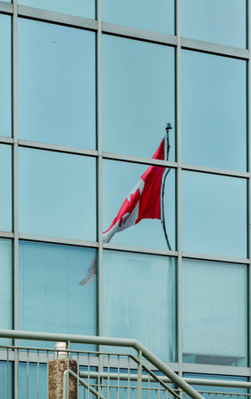 A Canadian flag reflected in a blue glass office building