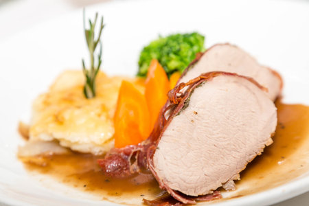 Sliced pork tenderloin with scallopped potatoes garnished with rosemary and vegetablesの写真素材