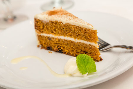 Slice of carrot cake on a white plate with dollop of whipped cream and mint leafの写真素材