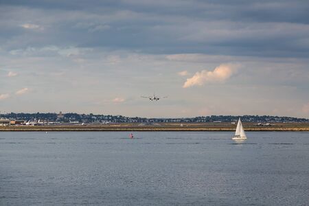 White Sailboats in Calm Blue Bay with Planes Landing at Airport in Backgroundの写真素材