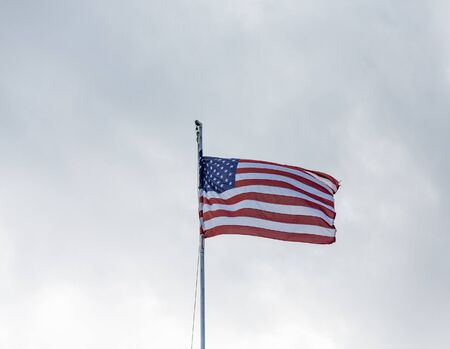 American Flag blowing in the wind at the top of a flagpoleの写真素材