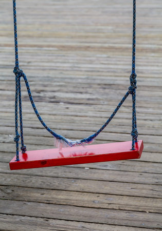 A red swing on a blue rope over wood deckの写真素材