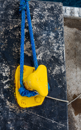 A blue ship's rope tied around a yellow cleat on black concrete pierの写真素材