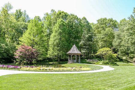 A gazebo and bridge in a public park surrounded by green lawnの写真素材