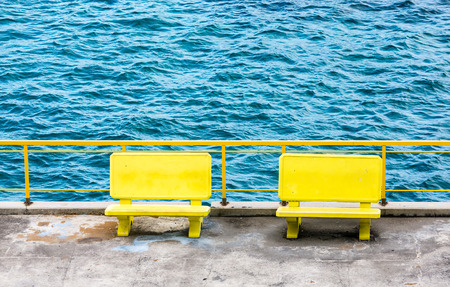 Two empty yellow benches on a pier by the blue seaの写真素材