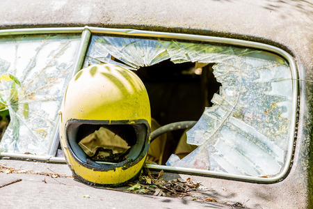 A yellow motorcycle helmet smashed through the window of a rusty old car in the woodsの写真素材